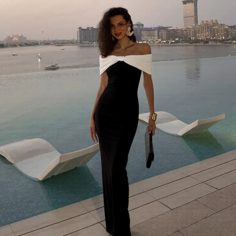 Woman in a black and white dress standing by an infinity pool with a cityscape in the background
