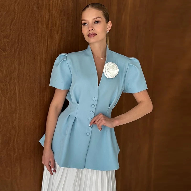 Woman wearing a light blue blouse with a white flower accessory against a wooden background