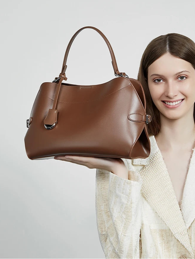 Woman holding a brown handbag against a light gray background