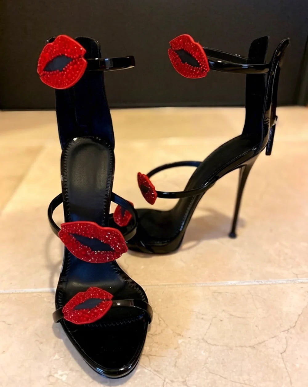 Black patent leather stiletto sandal with red lip embellishment and multi-strap design