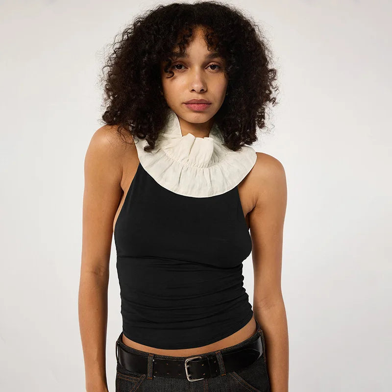 Woman wearing a black sleeveless top with a white ruffled collar against a plain background