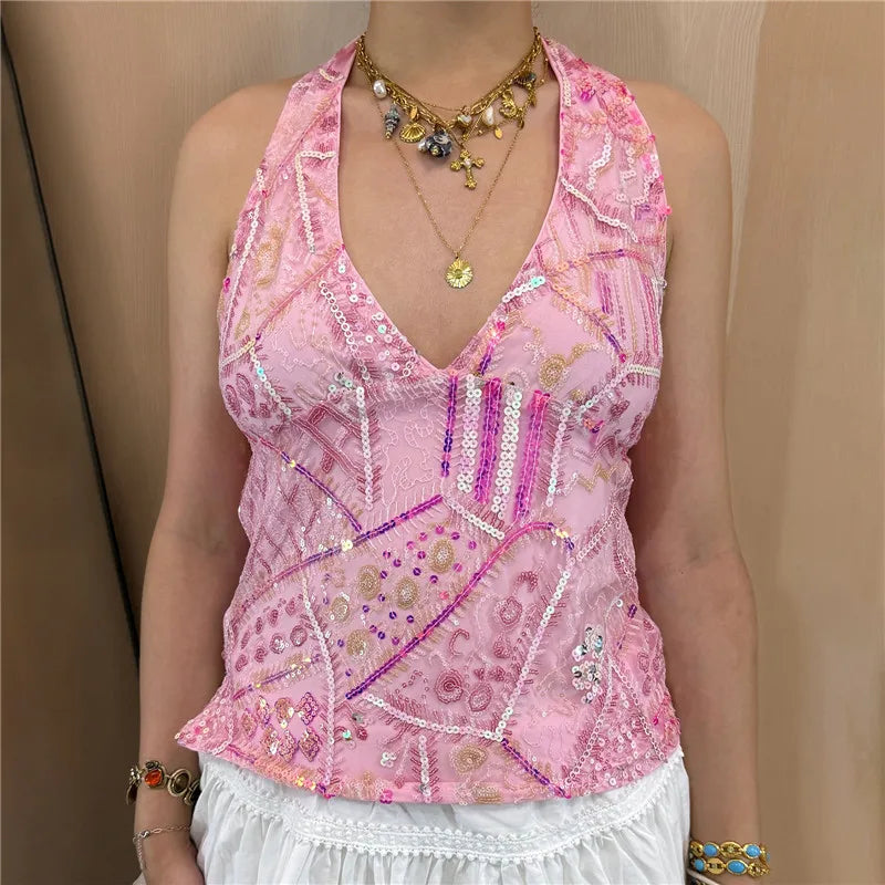 Person wearing a pink embroidered top with jewelry against a beige background