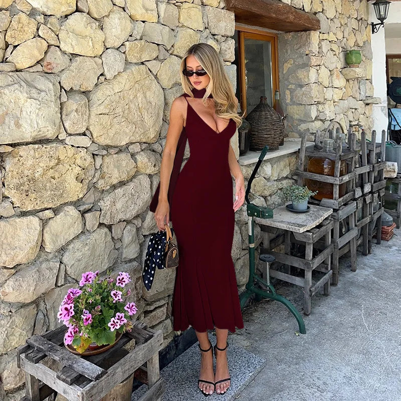 Woman in a burgundy dress standing against a stone wall with decorative elements.