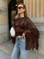 Woman wearing a sheer brown top and blue jeans standing outside a building.