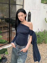 Woman wearing a navy one-shoulder top and jeans outdoors.