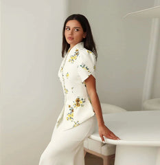 Woman wearing a white floral blouse and pants in a minimalistic setting
