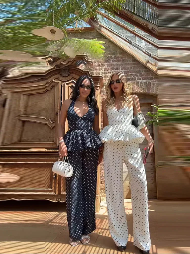 Two women in matching polka dot outfits standing in front of a decorative wall.