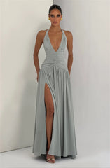 Woman wearing a silver halter neck gown with a high slit on a plain background