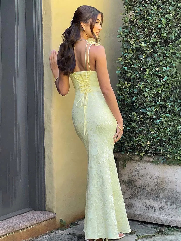Woman in a light green dress standing against a wall with greenery.