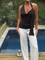 Person wearing a black polka dot top and white pants by a pool