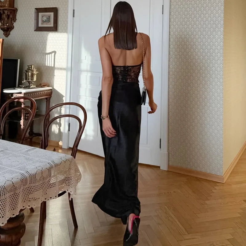 Woman in a black dress standing in a room with wooden floor and furniture.