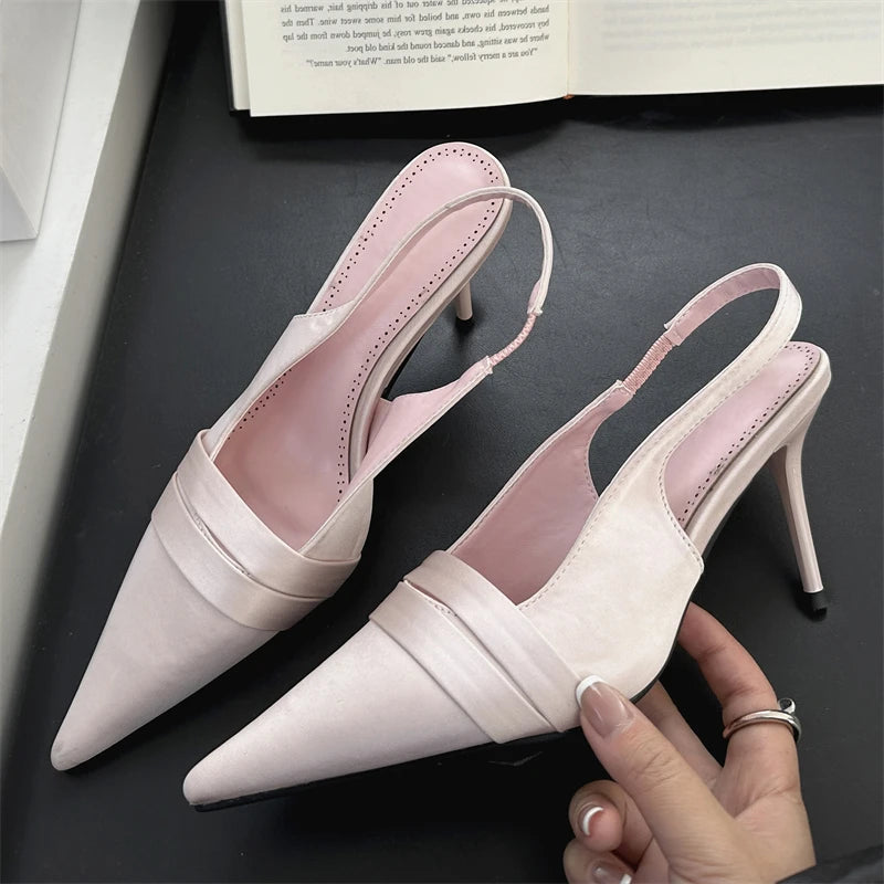 Pair of light pink heeled shoes on a dark surface with a book in the background.