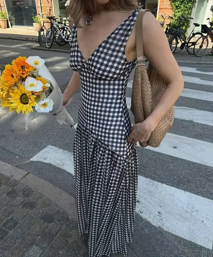 Woman in a black and white checkered dress holding flowers on a street.