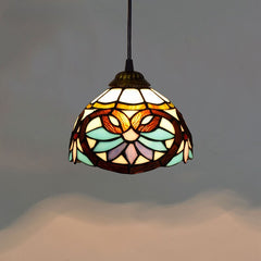 Golden Atelier pendant light featuring a handcrafted Tiffany glass shade with colorful stained glass panels, casting a warm glow. The light hangs from a chain on a ceiling in a living room setting. B 