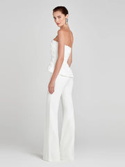Woman wearing a white strapless jumpsuit on a light gray background