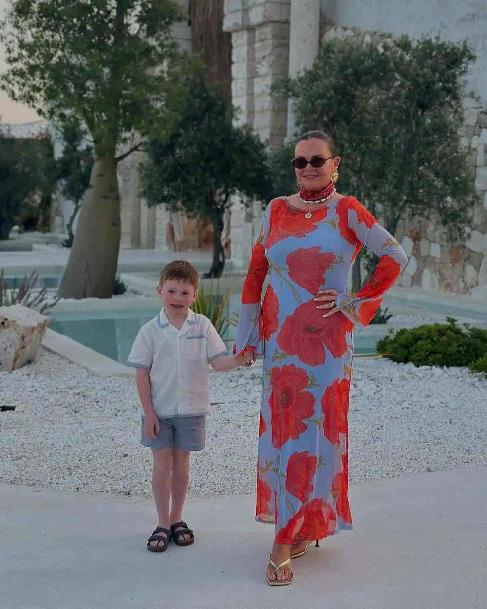 Woman in a colorful dress and child standing in front of a stone archway with 'PYRAMIS' inscribed.