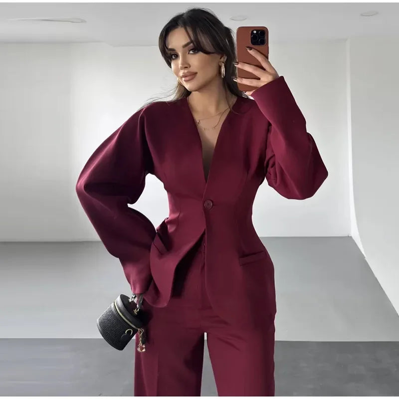 Woman in a burgundy suit taking a mirror selfie in a minimalistic setting