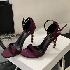Pair of purple high-heeled sandals with gold accents on a white surface.