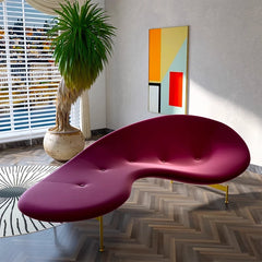 Sculptural purple sofa with golden legs and potted plant beside window