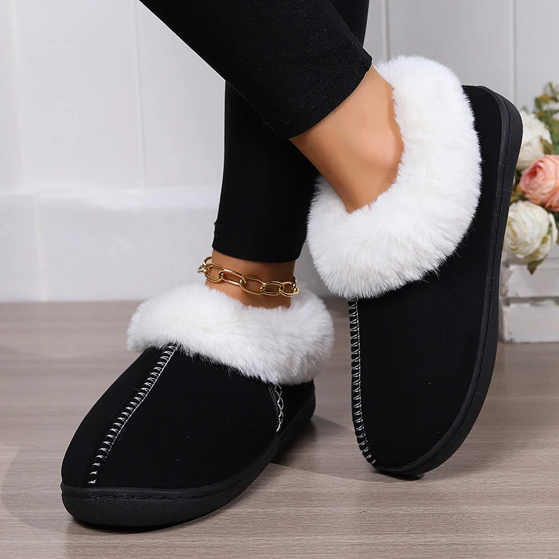 Black slippers with white fur lining worn by a person on a wooden floor.