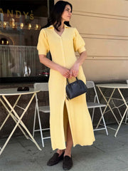 Woman in a yellow dress holding a black handbag outdoors.