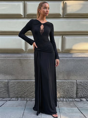 A woman in a black twisted neck ruched waist maxi dress standing against a stone wall