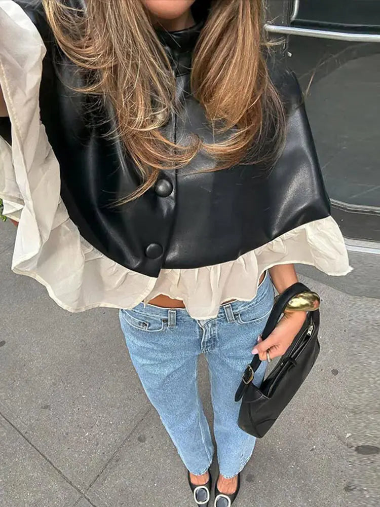 Person wearing a black leather vest over a white shirt with blue jeans, holding a black handbag.