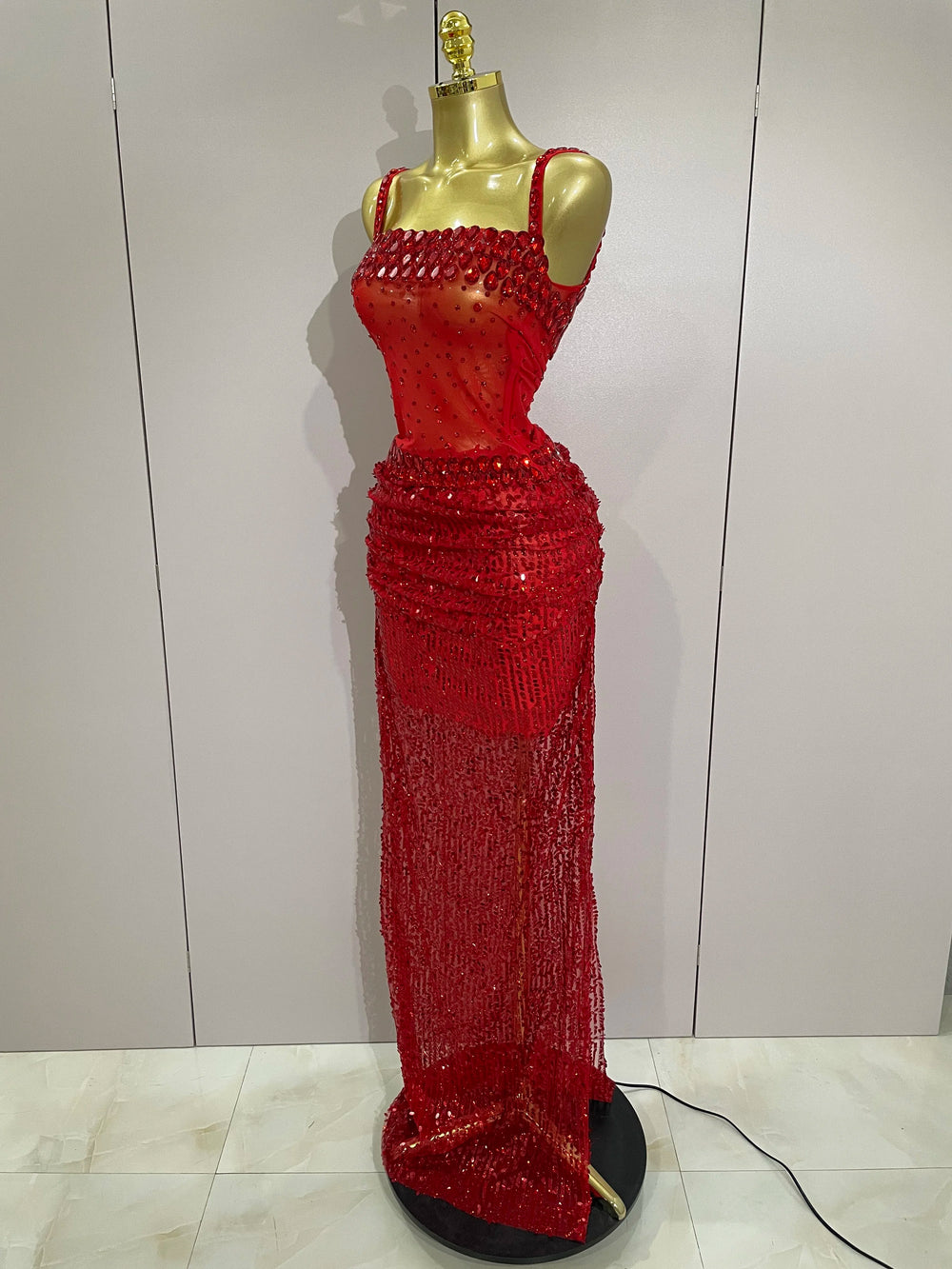 Red beaded evening gown on a mannequin against a white wall.