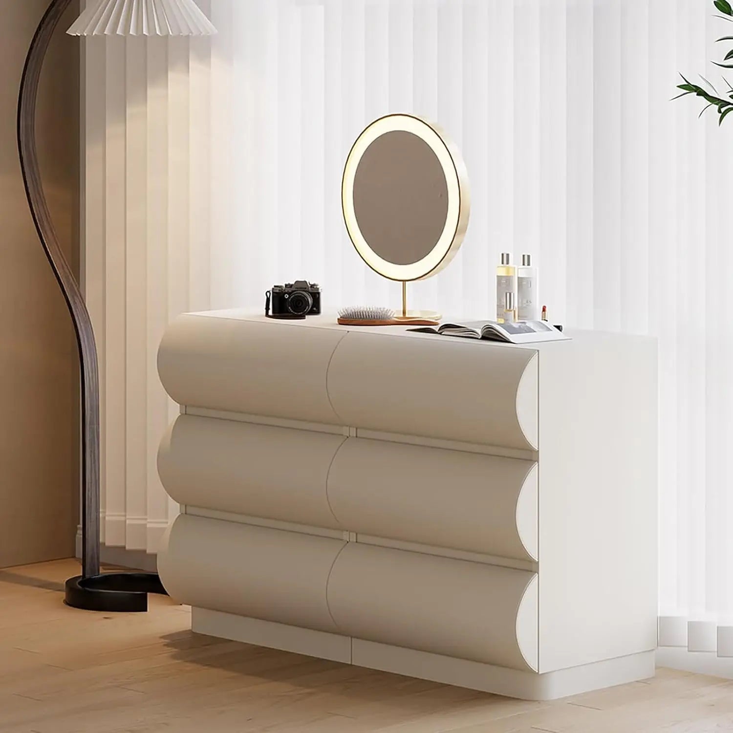 Beige dresser with a round mirror and various items in a room with light-colored walls and a lamp.
