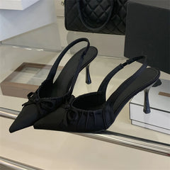 Black heeled shoes with bow details on a reflective surface