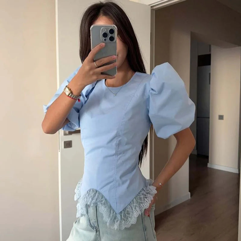 Person wearing a light blue top with puffed sleeves and lace details, taking a mirror selfie.