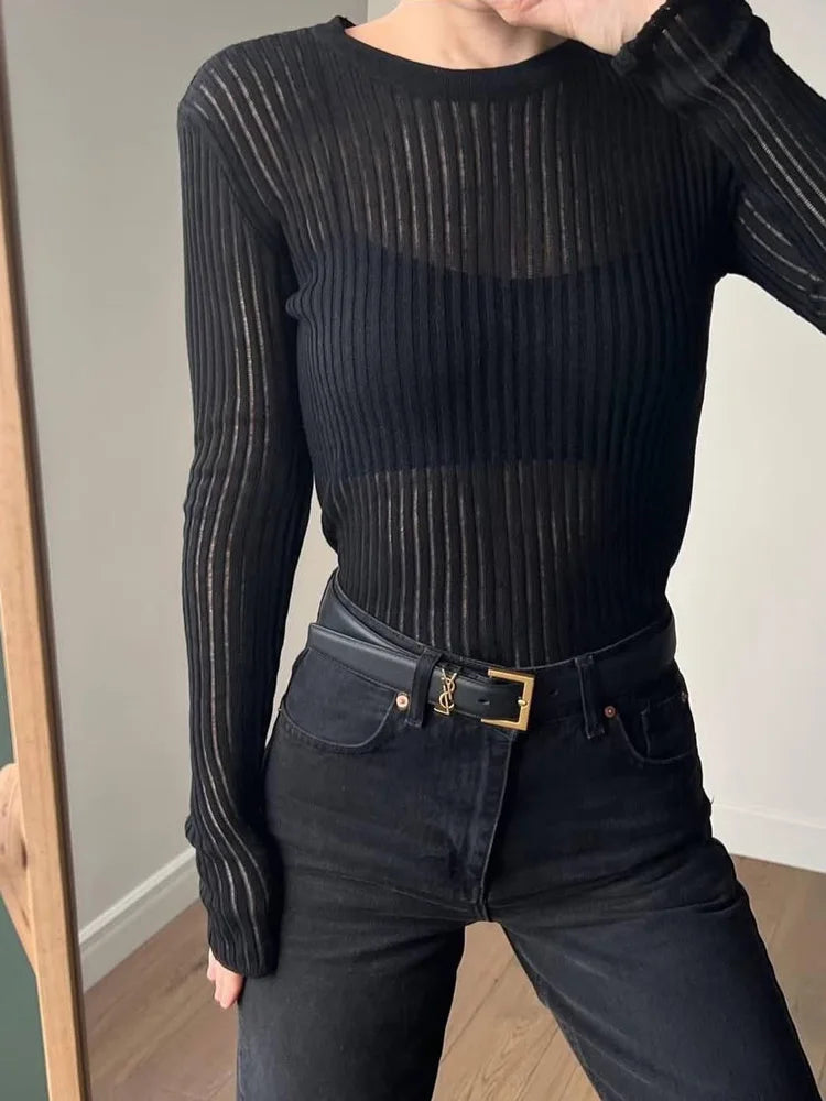 Person wearing a black ribbed long-sleeve top and dark jeans with a belt, standing in front of a mirror.
