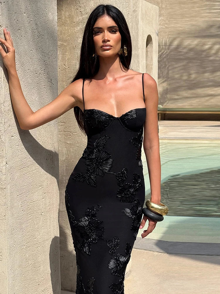 Woman in a black floral dress standing against a stone wall.