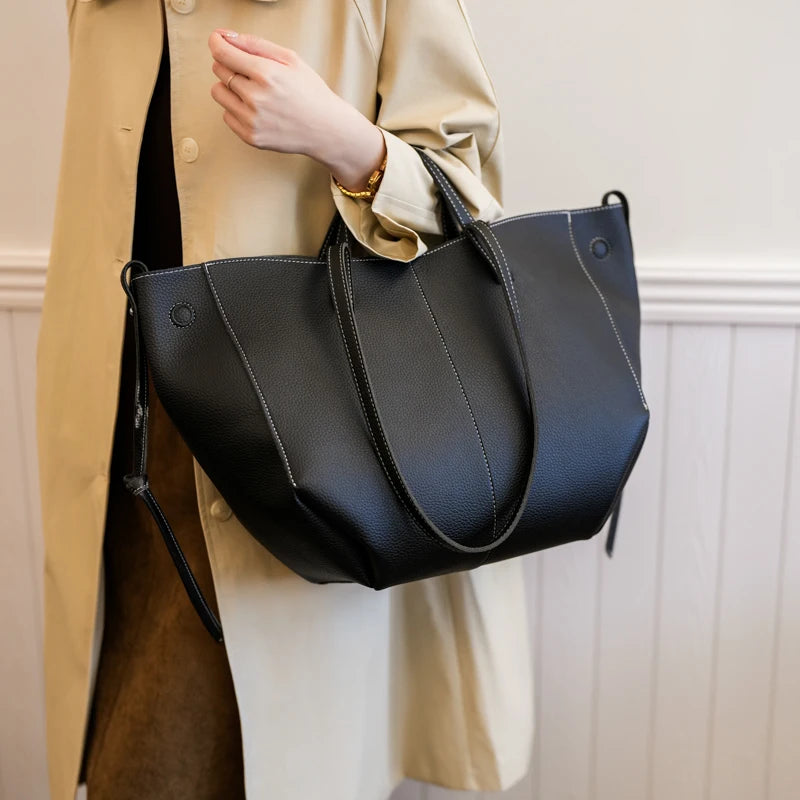 Person holding a black handbag against a neutral background