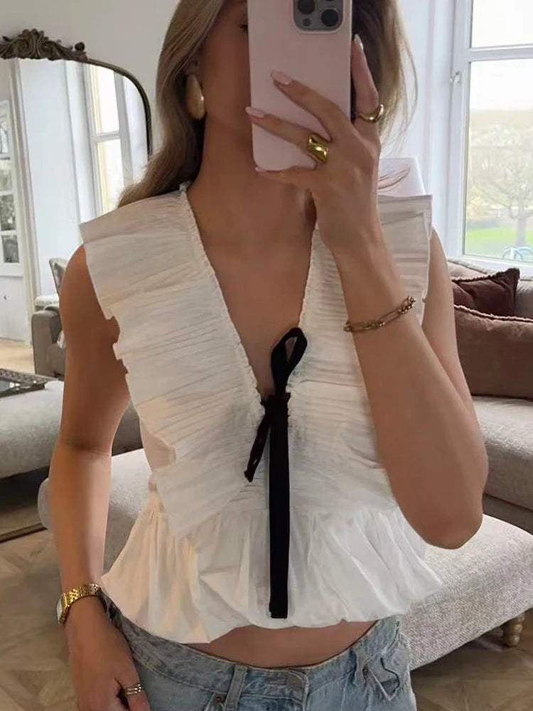 Sleeveless peplum top with a deep V-neckline, pleated collar, and a black bow tie detail.