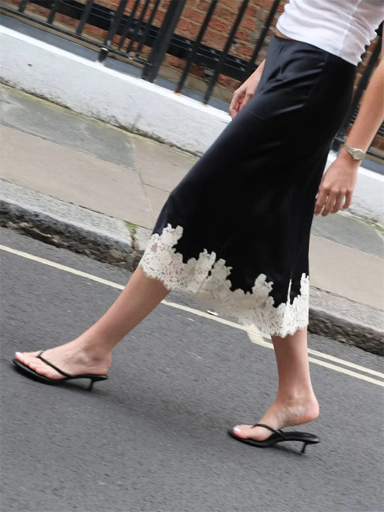 Person wearing black pants with white lace trim walking on a street.