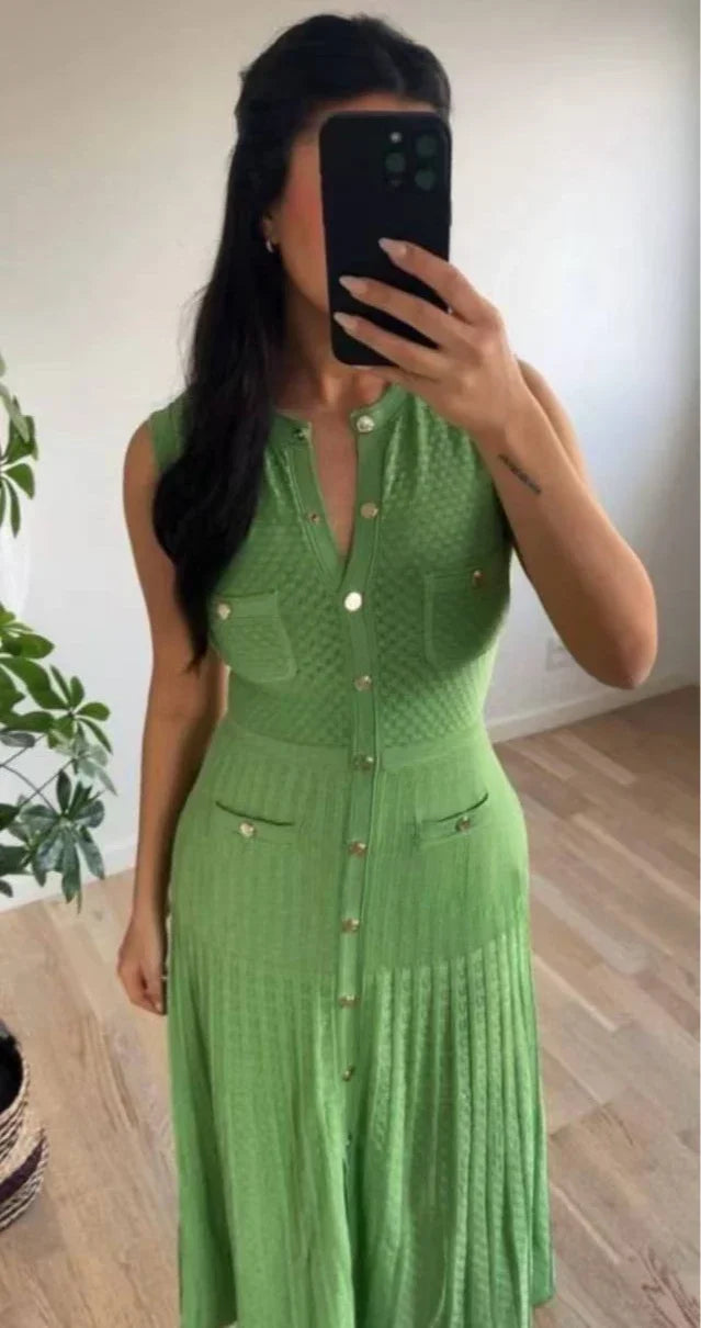 Woman wearing a green dress taking a mirror selfie indoors.