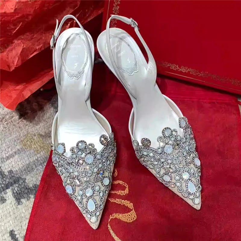 Pair of white high-heeled shoes with decorative embellishments on a red surface.