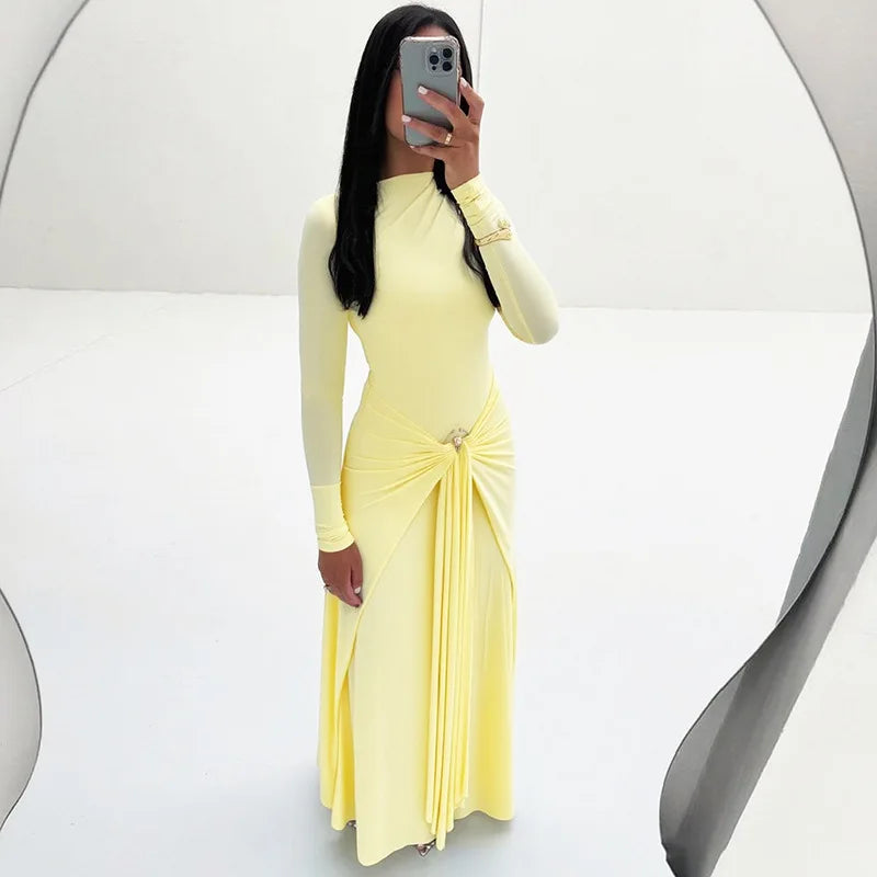 Person wearing a yellow long-sleeve dress with a slit, standing against a white background.