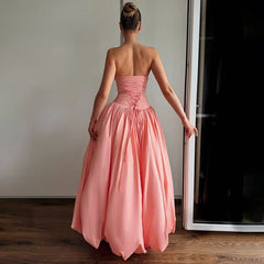 Woman wearing a pink strapless gown standing in a room with a white wall and wooden floor.