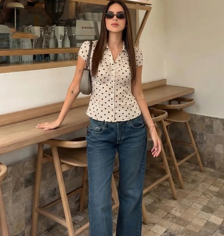 Woman in a polka dot shirt and jeans standing in a cafe.