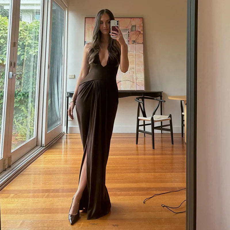 Woman taking a mirror selfie wearing a long dark dress in a room with wooden flooring and large windows.