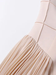 Close-up of a beige dress with pleated skirt on a light gray background