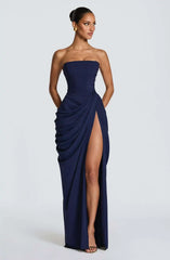 Woman wearing a strapless navy gown with a high slit on a white background