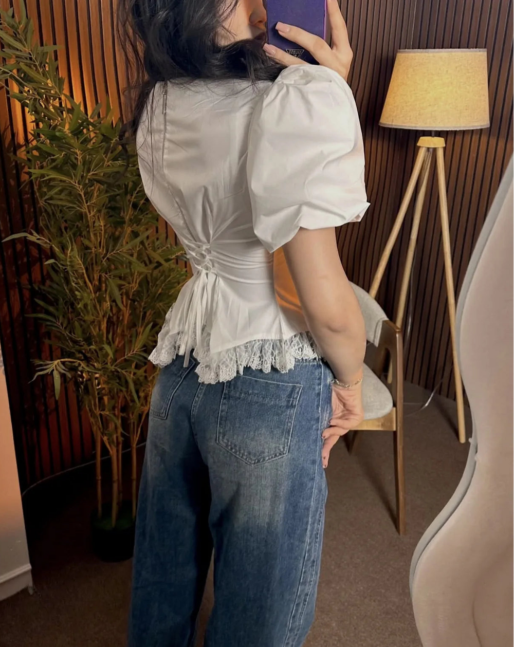 Person wearing a white blouse with puffed sleeves and blue jeans indoors.