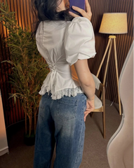 Person wearing a white blouse with puffed sleeves and blue jeans indoors.