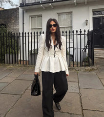 Woman in a white peplum top and black pants walking on a pavement.