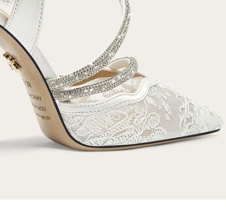 White high-heeled shoe with lace detailing and a decorative strap on a white background