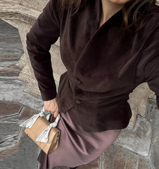 Person wearing a brown coat and holding a beige handbag on a stone pavement.