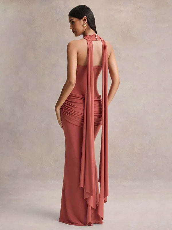 Woman wearing a long, elegant dress with a draped design on a neutral background